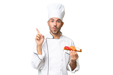 Young caucasian chef holding a sushi over isolated background intending to realizes the solution while lifting a finger up