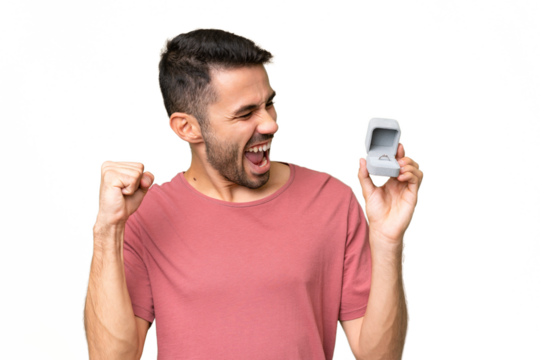 Young handsome caucasian man holding a engagement ring over isolated background celebrating a victory