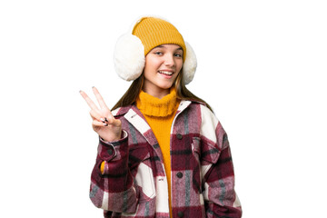 Teenager caucasian girl wearing winter muffs over isolated background smiling and showing victory...
