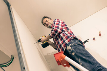 Home renovation - happy handyman (contractor) installs gypsum boards walls (plasterboards, drywalls) using a drill driver.