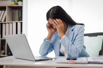 Businesswoman working with laptop in office, she is seriously working, is stressed and tired. Asian...