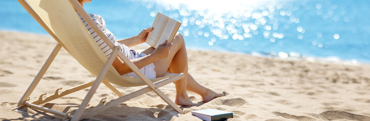 Woman sitting with book in the chaise lounge on the sea beach.