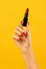 Unrecognizable slim young woman holding lipstick in hand against yellow backdrop