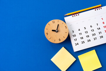 Obraz premium close up of calendar and clock on the blue table background, planning for business meeting or travel planning concept