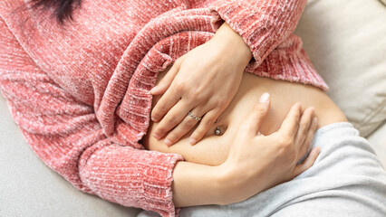 Woman with intense stomach pain lying on the couch. Stomach ache. Woman with stomach pain due to constipation, menstruation, woman suffering and holding her belly in a living room, close up view