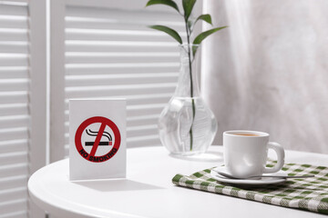 No Smoking sign and cup of coffee on white table indoors