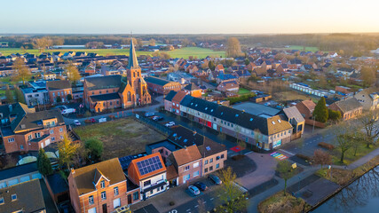 This aerial shot captures the quaint town of Rijkevorsel during the soft light of dusk. The Sint Jozef Church, with its towering spire, stands prominently among the surrounding residential buildings - obrazy, fototapety, plakaty