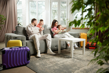 Family, parents with children sitting on couch and preparing for tour and choose hotel online in...