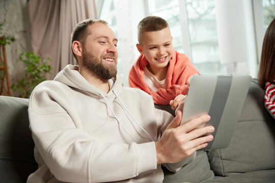 portrait of man, dad shows child, his son, something on tablet while sitting on couch in living room at home. Concept of tourism,booking services, holiday, vacation, journey, relaxation. Ad