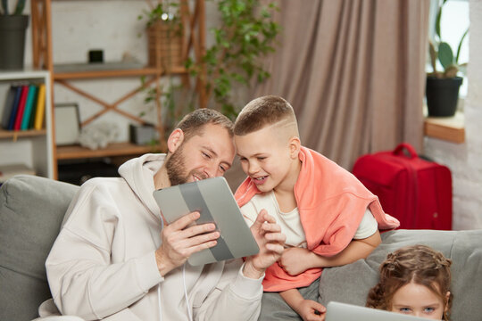 Photo of father with son, man with boy looking at tablet and smiling while little girl sitting with laptop. Concept of tourism, holiday, adventures and journey, vacation, relaxation. Ad