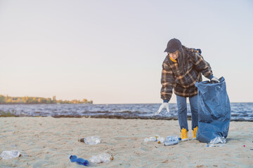 Young girl picking up trash and plastics cleaning the beach with a garbage bag. Eco-activist...