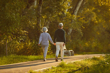 Backside view of a senior family couple enjoying a stroll hand in hand through the city park. Their active vacation showcases the beauty of shared moments and the fulfillment found in simple walk.
