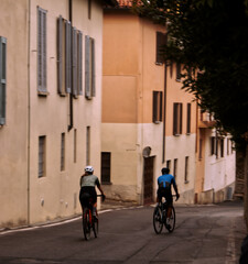 Fototapeta na wymiar Two cyclists pedal through the streets of Lombardy.