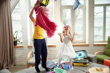 Two kids, boy and girl jumping on bed and having fun throwing things in different directions when preparing for trip. Concept of tourism, travel agency, holiday, family resort, vacation, relaxation. - obrazy, fototapety, plakaty