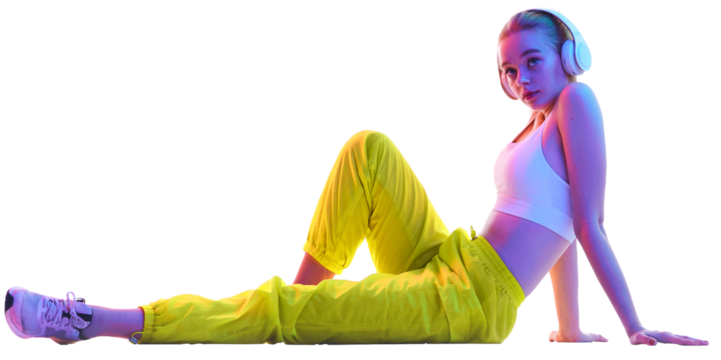 Side view portrait of young girl sitting on floor in trendy sport outfit and headphones looking away in neon against transparent background. Concept of sport, fashion, active lifestyle, youth. Ad