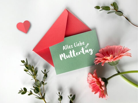 A photo featuring a green envelope placed next to a red envelope amidst vibrant pink flowers.
