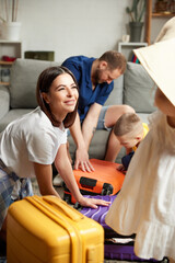 Man, woman, boy and girl preparing for travel, and packaging bags in bright living room. Joyful...