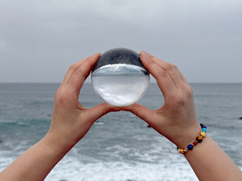 Hands holding crystal ball on ocean shore, meditation, spiritual journey, connection with Nature.
