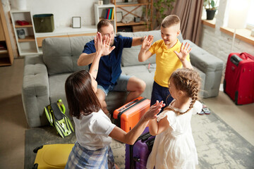 Parents and children packing backpacks at home, giving high five, standing in living room with...