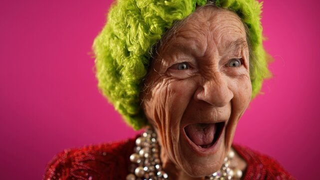 Smiling happy fisheye view of successful funny elderly woman with no teeth and green hat isolated on pink background. Caricature of peoples emotions