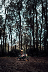 Naklejka premium Hombre moreno con moto dentro de un bosque posando y montando por terreno silvestre