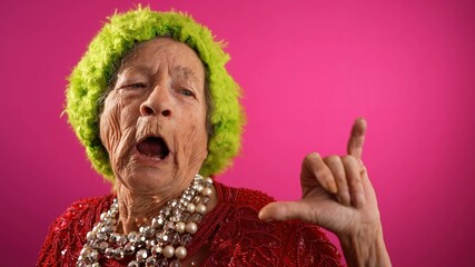 Fisheye view of funny elderly mature woman, 80s, wearing green wig giving SHAKA hand gesture...