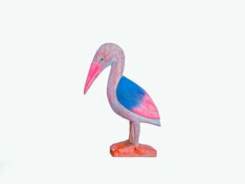 In the picture is a bird's-eye view made from teak, carved into the shape of a bird with a long pink beak, blue wings and a pink bottom, standing on a golden teak base.