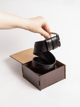 Genuine leather belt in wooden box on white background. Woman pulls out a belt