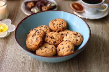 Easter eggs in the basket, bowl of cookies, chocolate pralines, Easter bunny figurine, cups of tea, glasses of juice, flowers and lit candles on the table. Selective focus.