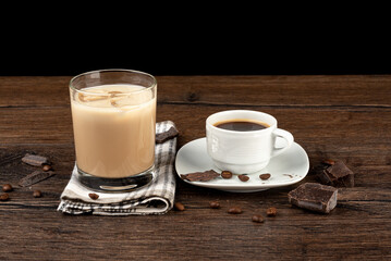 Coffee beans with chocolate pieces, a cup of coffee and a glass of Irish cream liqueur in a glass with ice.