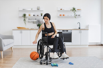 Cheerful beautiful woman with mobility impairment dribbling ball in studio apartment on weekend....