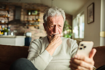 Worried senior man using a smartphone on the sofa at home