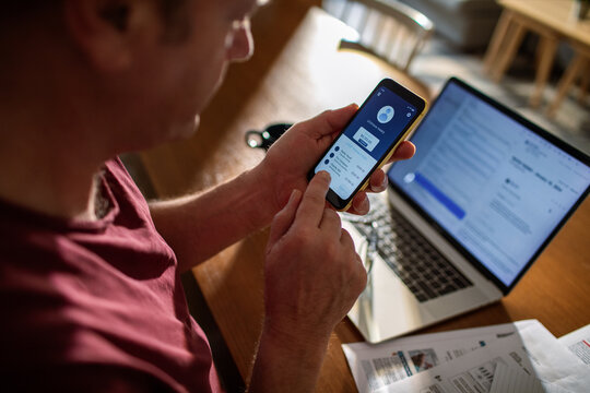 Back view of a man using bank smartphone app at home - Powered by Adobe