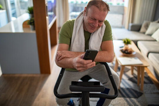 Middle aged man using smartphone on home exercise bike