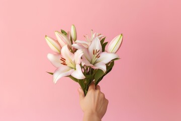 Close up woman's hand holds a bouquet of delicate pink lilies, set against a complementary pink background for a monochromatic effect