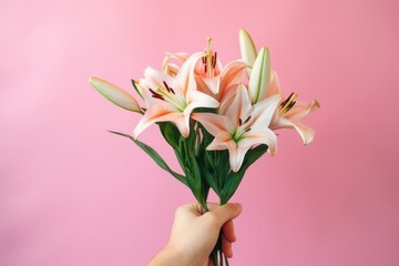 Close up hand tenderly holding a vibrant bouquet of lilies, exuding a cheerful and loving atmosphere against a pink background