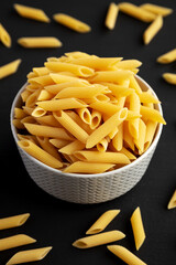 Organic Dry Penne Pasta in a Bowl on a black background, side view.
