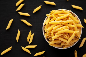 Organic Dry Penne Pasta in a Bowl on a black background, top view.