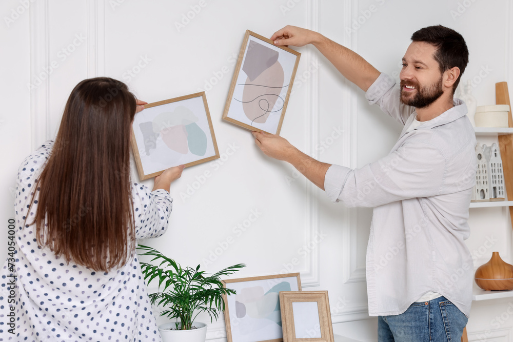 Poster Man and woman hanging picture frames on white wall at home