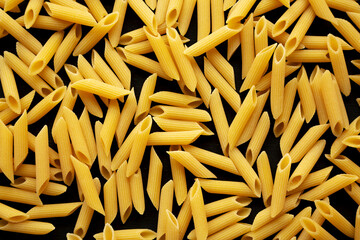Organic Dry Penne Pasta in a Bowl on a black background, top view. Flat lay, overhead, from above.