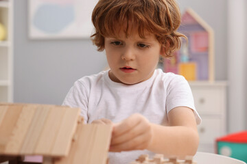 Little boy playing with wooden construction set in room, closeup. Child's toy