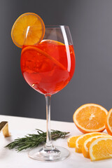 Glass of tasty Aperol spritz cocktail with orange slices and rosemary on white table against gray background