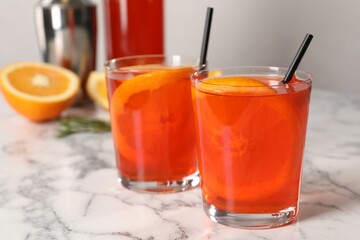 Aperol spritz cocktail, orange slices and straws in glasses on white marble table, closeup