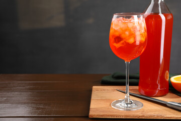Aperol spritz cocktail and ice cubes in glass and bottle on wooden table, space for text