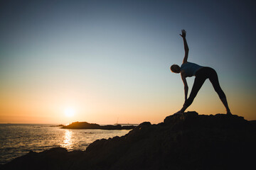 A woman exercising on the coast during sunset.
