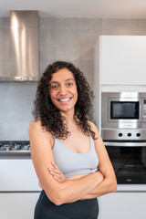 Vertical portrait of a young Spanish woman, Hispanic Latina, in the kitchen wearing workout attire - concept portrait of a brunette woman with curly hair