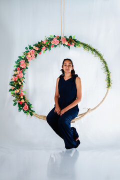 Mulher sentada em arco de flores para ensaio fotográfico em estúdio olhando para frente