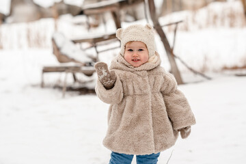 Obraz premium Cute little baby child toddler in a plush hat and fur coat on a snowy winter landscape with reeds. A cozy winter season, an active childhood, the baby looks like a teddy bear