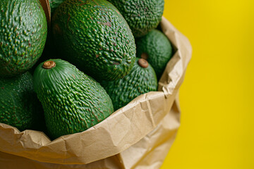 Fresh organic avocado in a paper bag on a yellow background. Healthy food concept and eco friendly lifestyle. Copy space. Close up.