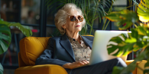 Senior businesslike old lady woman using laptop on a tropical luxury beach resort. Mature businesswoman in suit working on computer on the beach. Freelance online remote work freedom concept